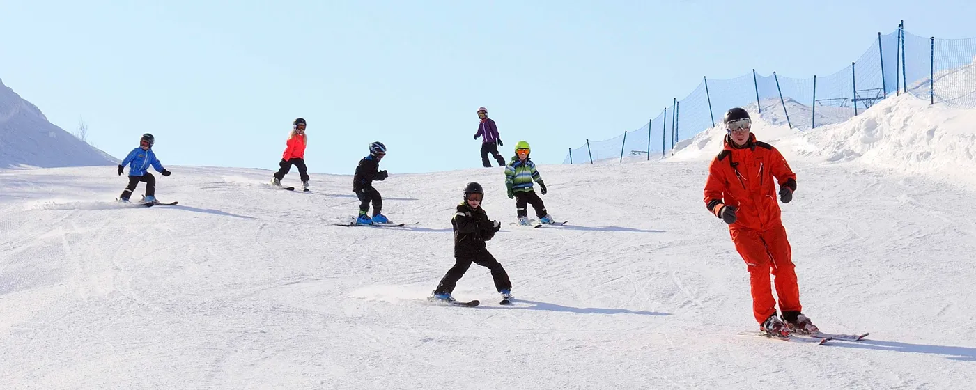 Skidlärare med en grupp barn som övar i en slalombacke..