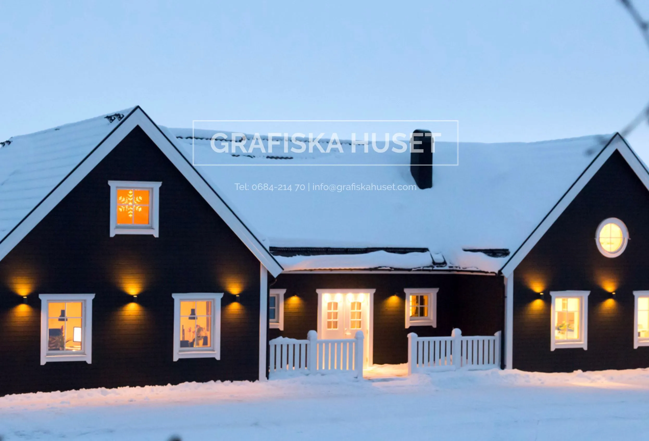 Grafiska huset vintertid, mörk träfasad med vitra fönsterfodet. Lampor som lyser.