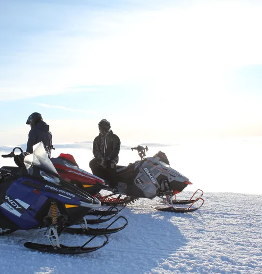 Två personer bredvid tre skotrar på fjället.