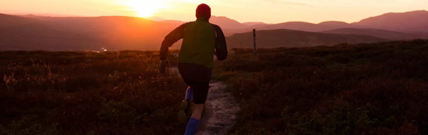 Man springer på fjället i solnedgången