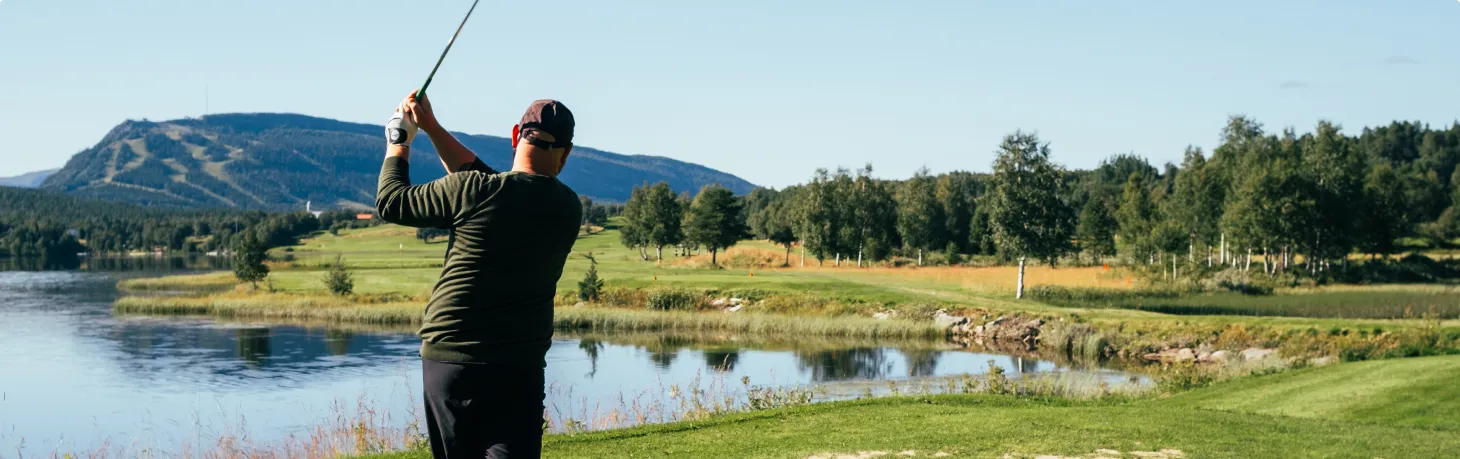 Person spelar golf med fjällen i bakgrunden