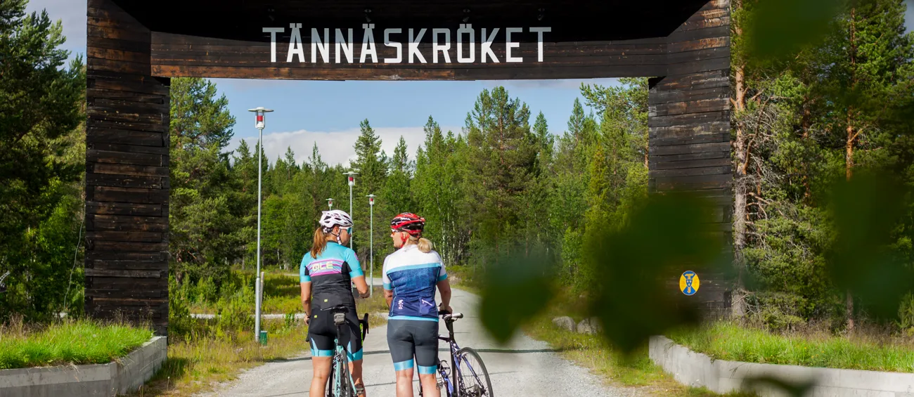 Cyklister på väg mot Tännäskröket - de står framför den stora träportalen